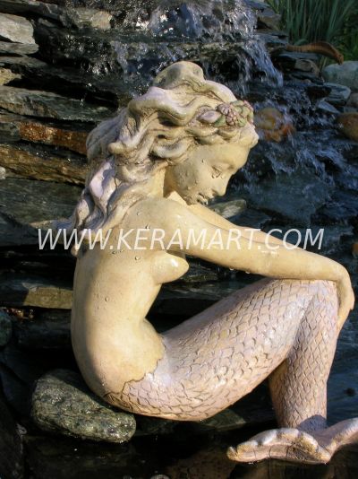 Садовая фигура -  русалка сидит на камне, обхватив руками хвост.
